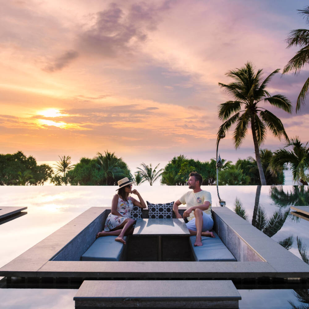 couple watching sunset in infinity pool on a luxury vacation in Thailand couple watching the sunset in an infinity pool on a luxury vacation in Thailand, man and woman watching the sunset on the edge of a pool in Thailand on vacation